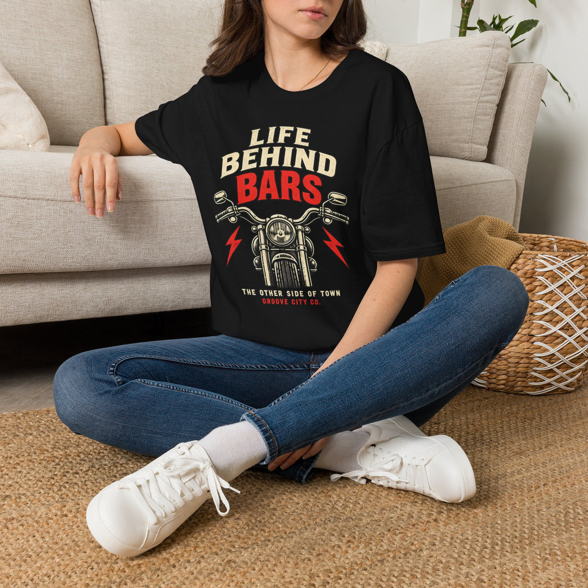 Woman seated indoors wearing a black “Life Behind Bars” motorcycle graphic T-shirt with red lightning bolts