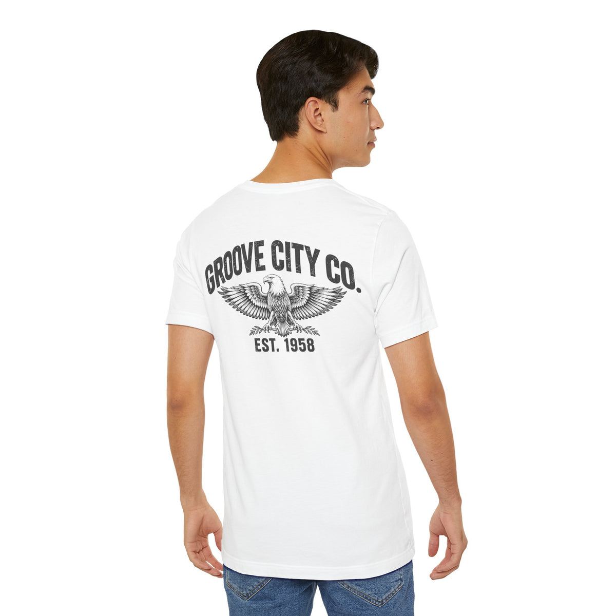 Male model wearing a white Groove City Co. vintage graphic T-shirt, showing the distressed American eagle back print with retro lettering and EST. 1958 design.