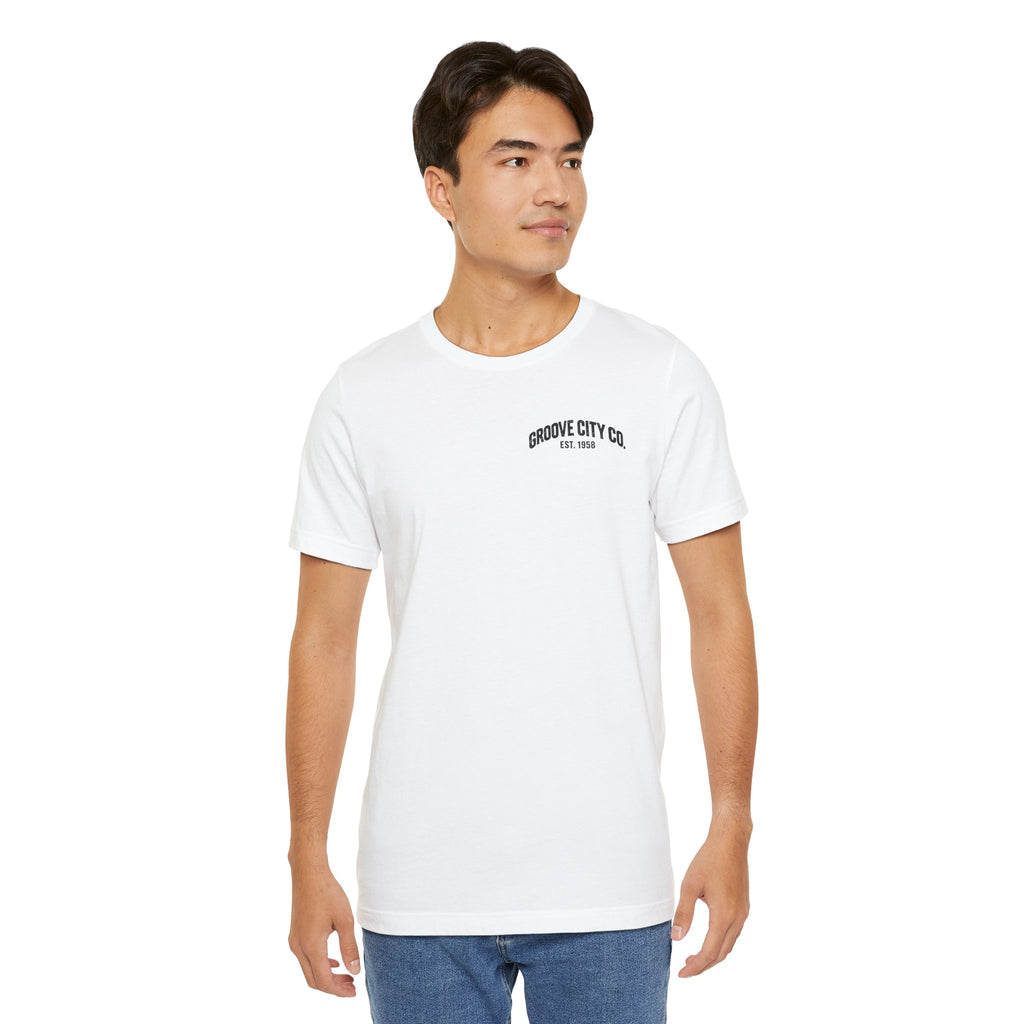 Male model wearing a white Groove City Co. vintage graphic T-shirt with a small retro chest logo, styled with blue jeans.