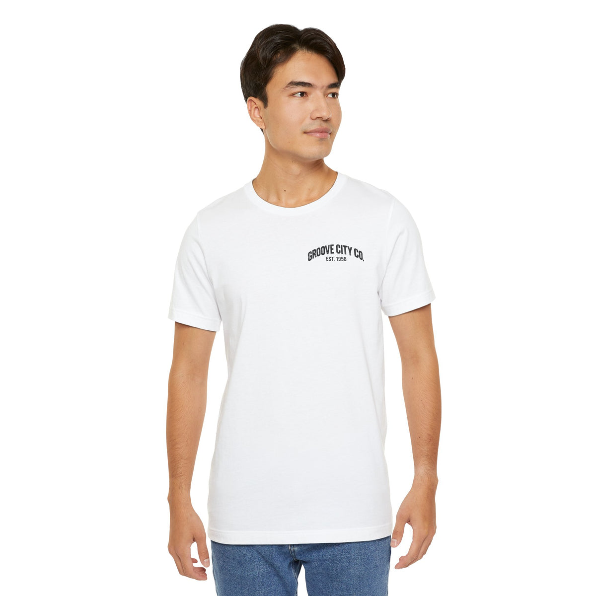 Male model wearing a white Groove City Co. vintage graphic T-shirt with a small retro chest logo, styled with blue jeans.