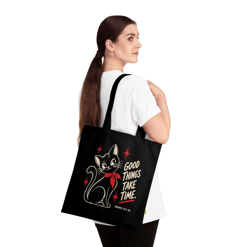 Woman carrying a black organic cotton tote bag with vintage cat artwork and Good Things Take Time lettering – Groove City Co.
